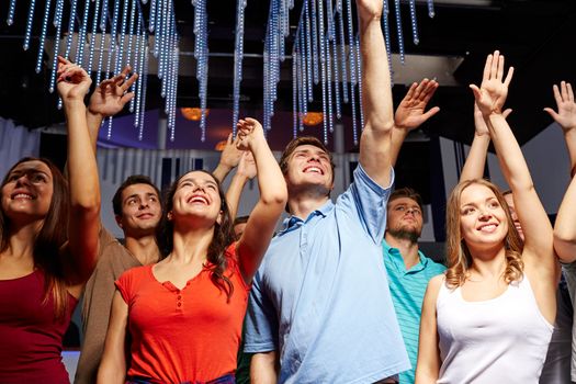 party, holidays, celebration, nightlife and people concept - group of smiling friends waving hands at concert in club