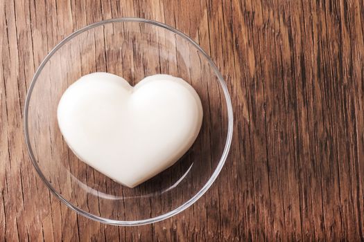 vanilla jelly in the form of heart on a glass saucer close-up on wooden background