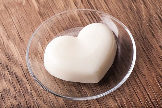 vanilla jelly in the form of heart on a glass saucer on wooden background