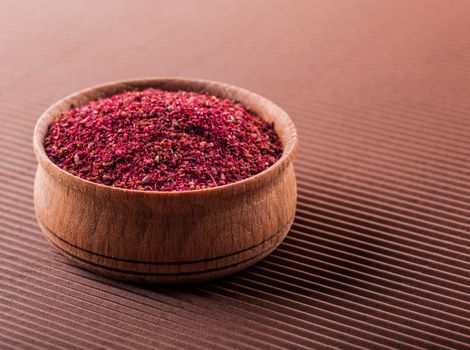 sumac in a wooden bowl on a brown background