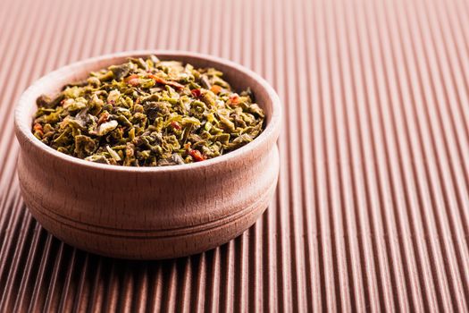 dry spice green pepper in a wooden bowl on a brown background