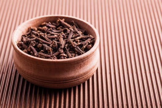 spice clove in a wooden bowl on a brown background