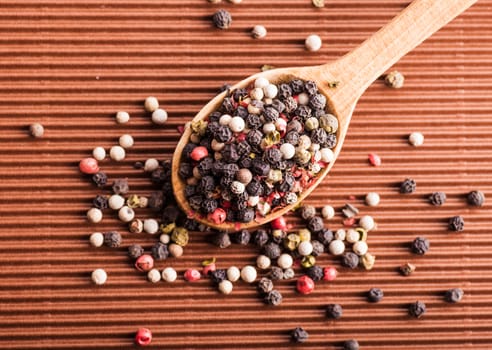 pepper in a wooden spoon on a brown background