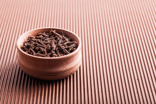 clove in a wooden bowl on a brown background