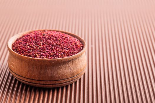 spice sumac in a wooden bowl on a brown background