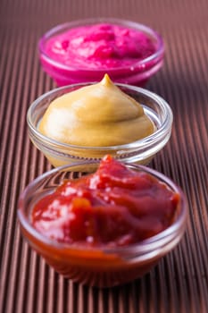 ketchup,mustard,horseradish in a glass bowl close-up on a brown background
