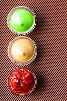 adjika,mustard,wasabi in a glass bowl close-up on a brown background