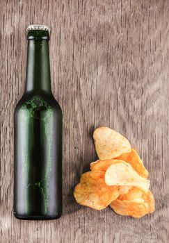 glass bottle of beer and chips on a wooden background