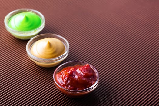 adjika,mustard,wasabi in a glass bowl on a brown background