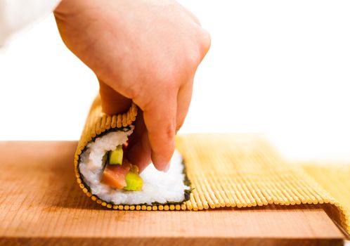 hand turns nori sheet with filling in the roll