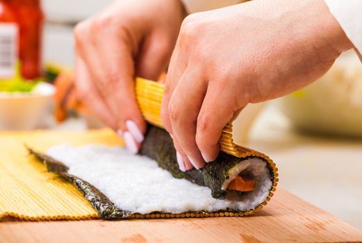 hands turns nori sheet with filling in the roll closeup