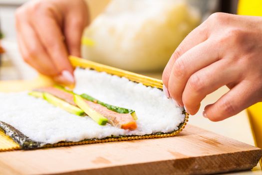 chef turns nori sheet with filling in the roll closeup