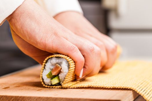 cook turns nori sheet with filling in the roll closeup