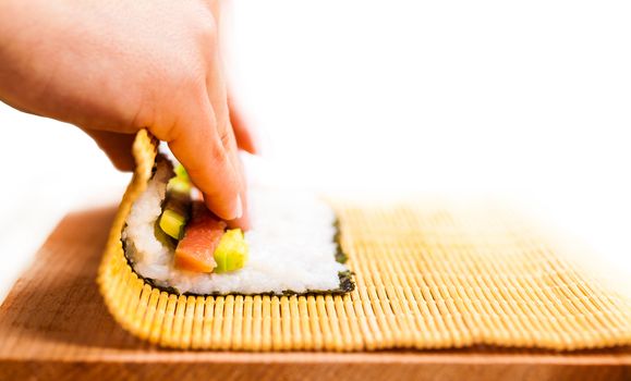 chef turns nori sheet with filling in the roll closeup