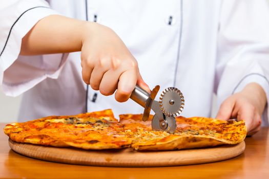 cook with a knife cuts the pizza closeup