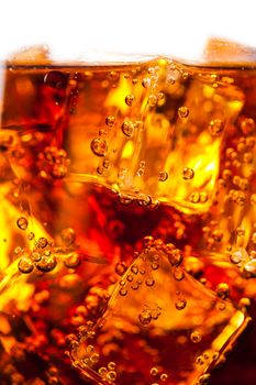 Cola with ice cubes and bubbles closeup