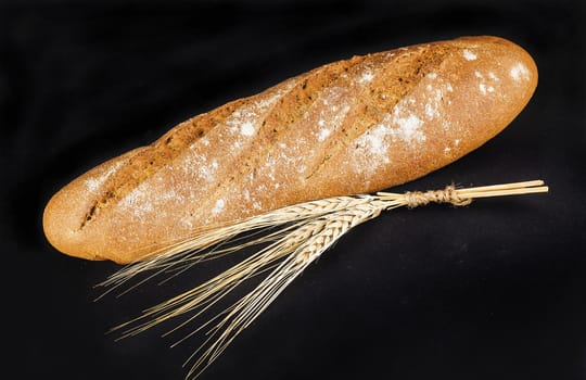 brown long loaf with ears of wheat on a dark background