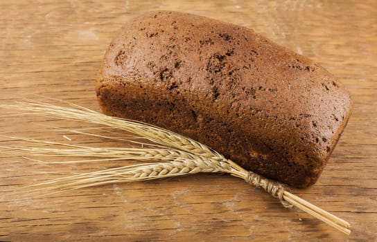 brown bread with ears of wheat on the wooden background