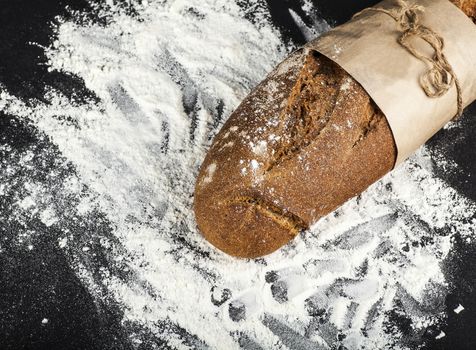 black long loaf on a dark background with flour