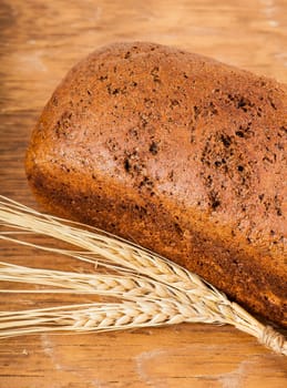 brown bread with ears of wheat closeup on wooden background