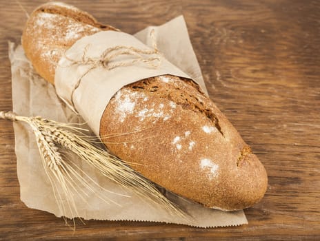 long loaf in paper packaging with ears of wheat on the wooden background