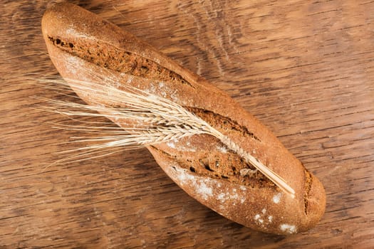 brown bread with ears of wheat on the wooden background