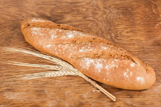 black bread with ears of wheat on the wooden background