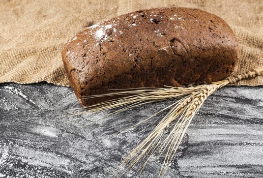 brown bread with ears of wheat on a dark background with flour