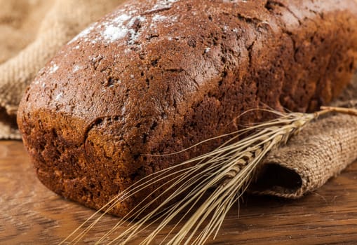 brown bread and ears of wheat closeup on wooden background
