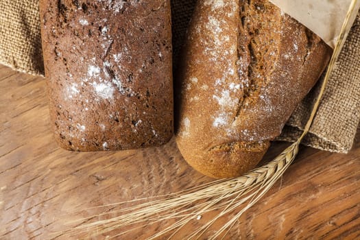 two black bread with ears of wheat on the wooden background