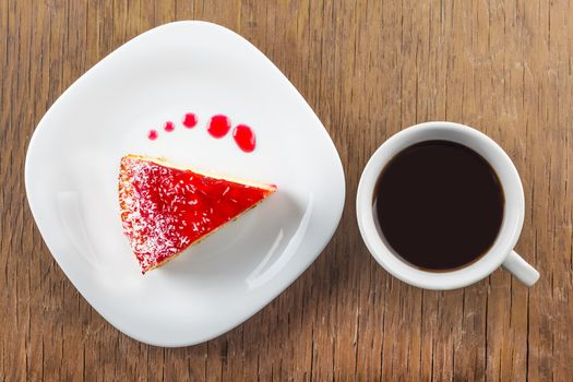a piece of cake and a cup of black coffee on a wooden background