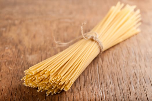 sheaf raw spaghetti tied with a rope on a wooden background