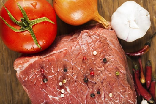 raw fillet of beef with spices and vegetables on wooden background