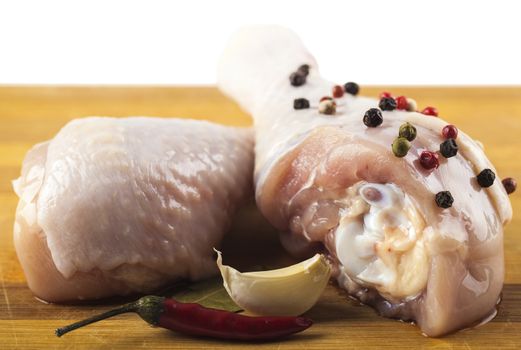 marinated chicken legs on a wooden board with spices, white background