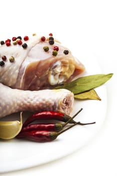 raw chicken legs on the plate with spices, white background