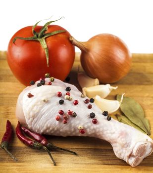 raw chicken leg on a wooden board with spices and vegetables, white background