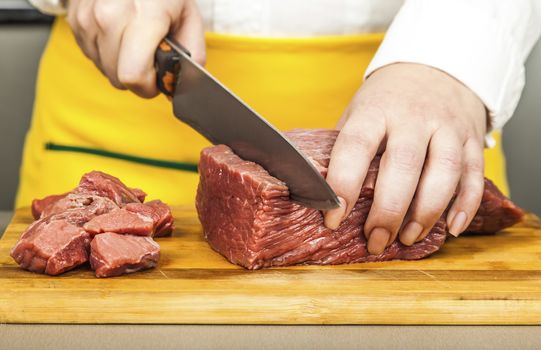 cook cuts meat fillet on a wooden board cubes