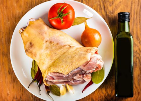 pork shank on a plate with spices and vegetables, a wooden background