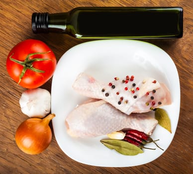 chicken legs on the plate with spices and vegetables, a wooden background