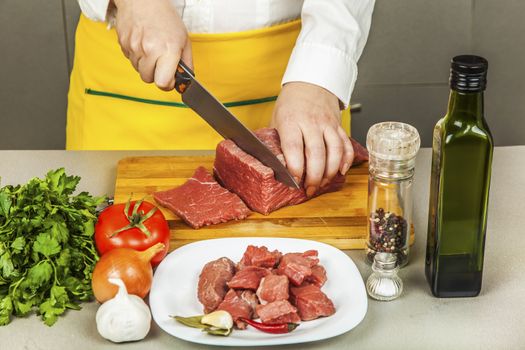 cook cuts meat fillet on a table with spices and vegetables