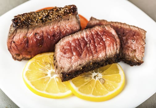Sliced grilled meat with slices of lemon on a white plate