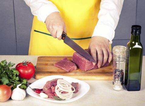 woman cuts meat fillet on a table with spices and vegetables