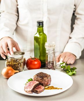 spices, vegetables and a dish of fried medallion on a background of cooks