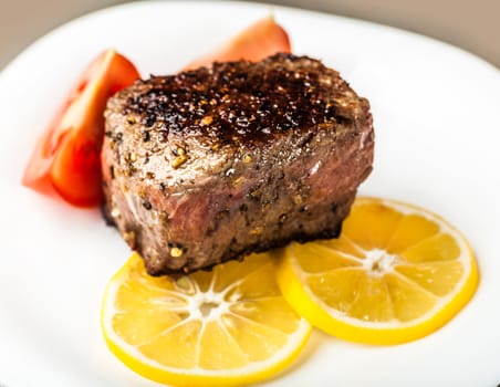 piece of roasted meat with lemon and tomatoes