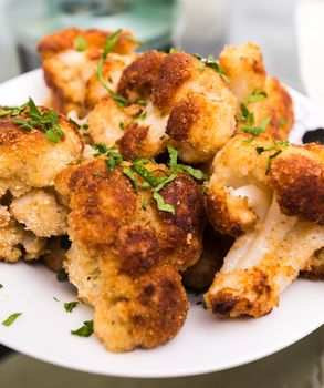 breaded and fried a cauliflower lying on a plate with greens