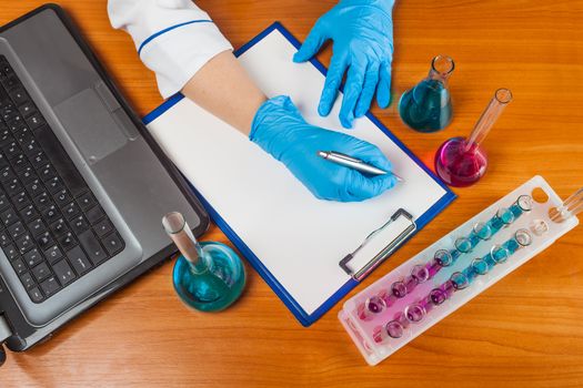 assistant of writes beside the laptop and test tubes with reagents 