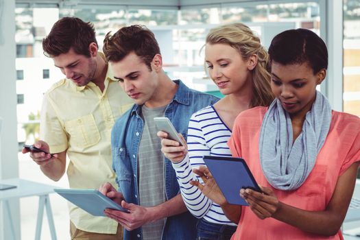 Smiling creative team standing in a line using technology in casual office