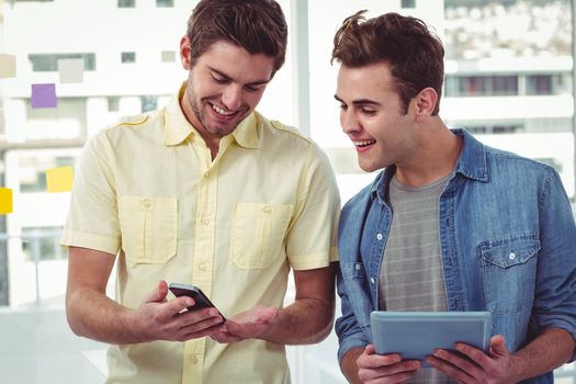 Smiling creative team standing in a line using technology in casual office