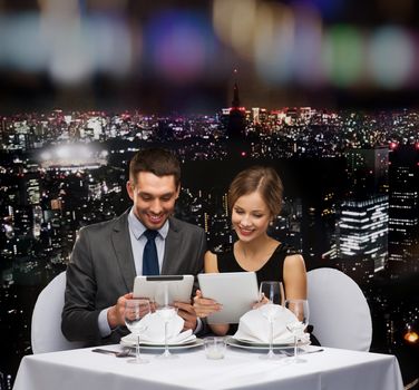 restaurant, couple, technology and holiday concept - smiling couple with menus on tablet pc computers at restaurant