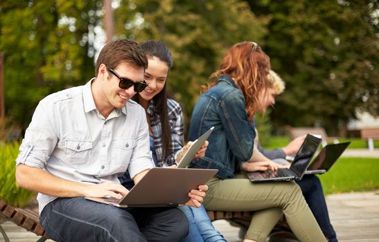 summer, education, technology and people concept - group of students or teenagers with laptop computers sitting on bench outdoors